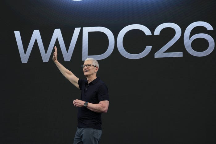 Tim Cook waves his right arm while standing on a stage with "WWDC26" in the background. Tim Cook waves his right arm while standing on a stage with "WWDC26" in the background.